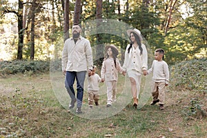 Young mother, father with daughter and sons are walking, having fun in autumn forest. Family holding hands enjoying time
