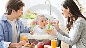 Young mother and father feeding baby son at kitchen