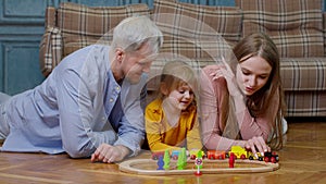 Young mother and father playing with child daughter riding toy train on wooden railroad game at home