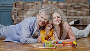 Young mother and father playing with child daughter riding toy train on wooden railroad game at home