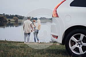 Young Mother and Father with Their Toddler Daughter Standing Outdoors Near the Lake, Concept of Family Road Trip on a