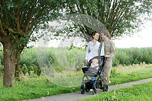 Young mother and father walking outdoors with baby in pram