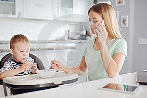Young mother feeding child and talking on the phone