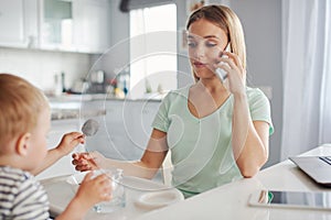 Young mother feeding child and talking on the phone