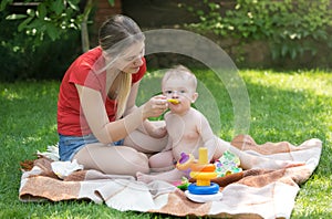 Young mother feeding her baby boy on picnic at park