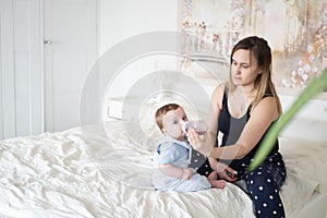 Young mother feeding her little baby boy from bottle in bed. mom gives her baby a drink