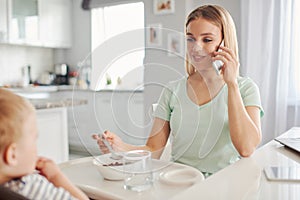 Young mother feeding toddler and speakingon the phone