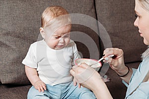 Young mother feeds the baby. Small baby refuse to eat food and crying over feeding time