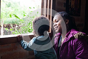 Young mother gazes lovingly at her little boy as he gazes ecstatically at the garden outside the window