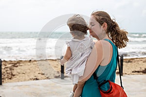 A young mother gently lovingly holds a baby girl in her arms against the background of the sea