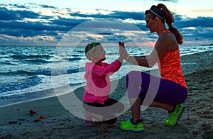 Young mother giving child high five on seacoast on sunset