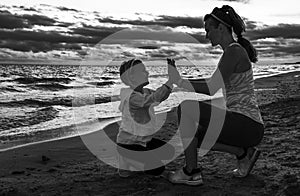 Young mother giving child high five on seacoast on sunset