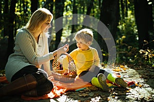 Young mother giving her little son a sweet season berrie at autumn picnic. Mum and kid sitting at picnic blanket and