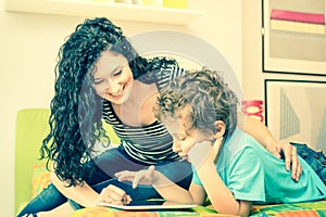 Young mother having fun learning with son using tablet on bed