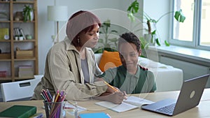 Young mother helping her son doing homework and sitting at table in home interior spbd.