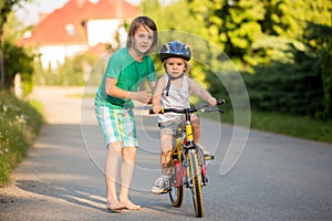 Young mother, helpOlder brother, helping his little brother to learn how to ride a bike, holding him and teaching him  bikinging