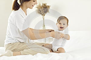 Young mother with her baby girl on weekend together relaxing and playing in cozy bright bedroom.