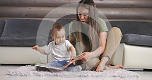 Young mother and her baby son play with book while sitting on floor at home. Mother play with little baby boy at home.