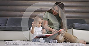 Young mother and her baby son play with book while sitting on floor at home. Mother play with little baby boy at home.