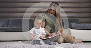 Young mother and her baby son play with book while sitting on floor at home. Mother play with little baby boy at home.