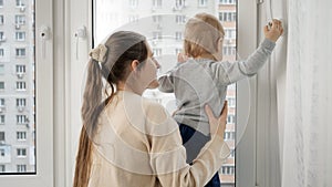 Young mother with her baby son walking out of the window at house