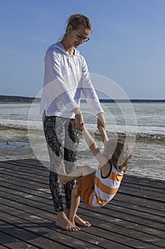Young mother with her child holding hands and doing exerciseon the beach.