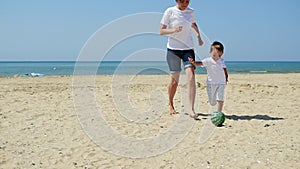 A young mother and her child are playing a ball on a sandy beach. Happy family are playing football. The concept of