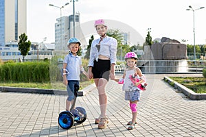 Young mother with her children son and daughter ride a skateboard and gyro scooter in the park