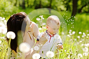 Young mother and her cute son blowing dandelion flowers together