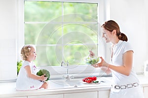 Young mother and her cute toddler daughter cooking