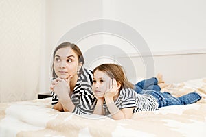 Young mother and her daughter child lying on bed in bedroom and watching tv together