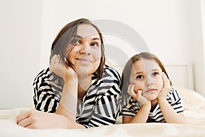 Young mother and her daughter child lying on bed in bedroom and watching tv together