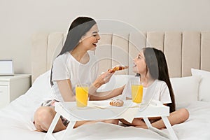 Young mother and her daughter having breakfast on bed