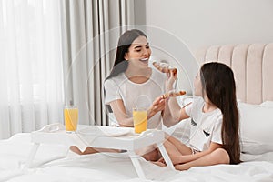 Young mother and her daughter having breakfast on bed