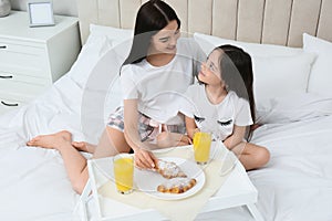 Young mother and her daughter having breakfast on bed at home