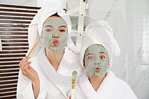 Young mother and her daughter with masks having fun in bathroom