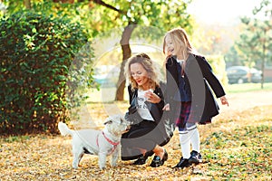 Young mother and her daughter playing with dog outdoors. Family, pet, domestic animal and lifestyle concept. Autumn time