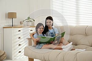 Young mother and her daughter reading book on sofa at home