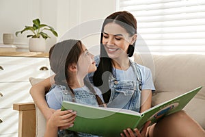 Young mother and her daughter reading book on sofa