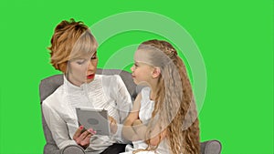 Young mother and her daughter sit together and look at the tablet on a Green Screen, Chroma Key