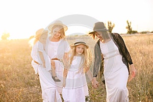 A young mother with her daughters and an aunt with blond hair in white dresses at sunset in the summer in a field of countryside. photo