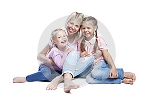 A young mother with her daughters smile and hug. Children with pigtails, in pink sweatshirts and jeans. Love and tenderness in a