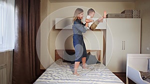 Young mother and her happy little boy jumping on big bed in bedroom