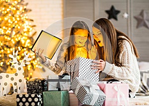 Young mother and her ittle daughters opening a magical Christmas