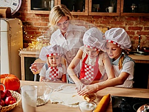 Young Mother with her Kids at the kitchen cook dough. Family relationships