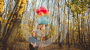 A young mother and her a little adorable daughter with the colorful balloons are walking in autumn forest.