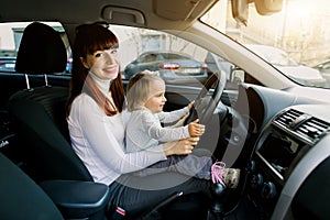 Young mother with her little baby girl sitting in the car in the front seat near car steering wheel. A woman and baby