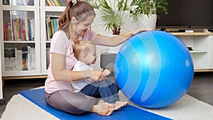 Young mother with her little baby son playing with fitball while doing fitness on mat at living room. Concept of healthcare,