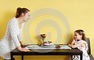 A young mother and her little daughter celebrate at home and enjoy a blueberry cake