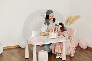 A young mother and her little daughter celebrate their birthday with a cake.